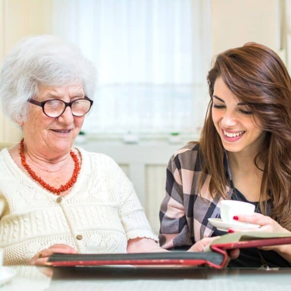 Young lady looking through family photo album with senior mother
