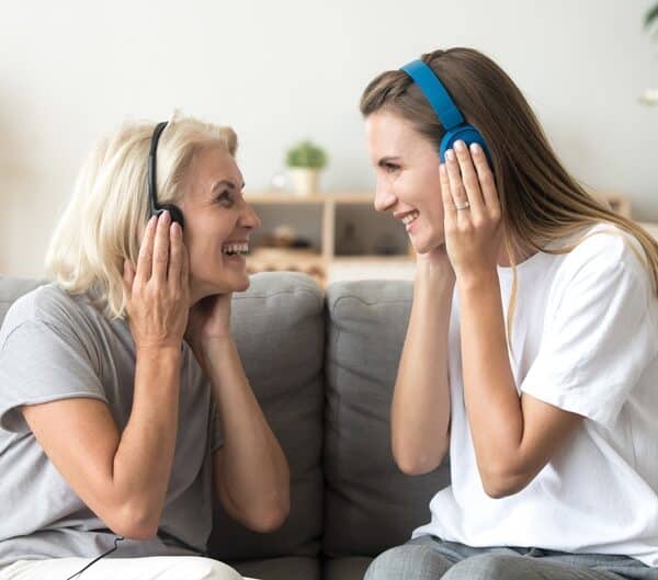 Daughter with elderly mother, each listening to headphones, sharing music