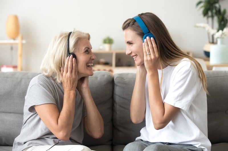 Daughter with elderly mother, each listening to headphones, sharing music