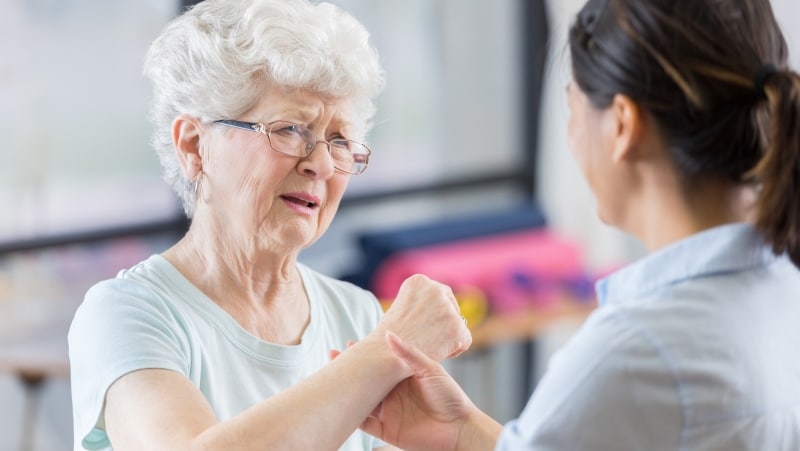 Elderly lady grimaces in pain as her therapist treats her arm